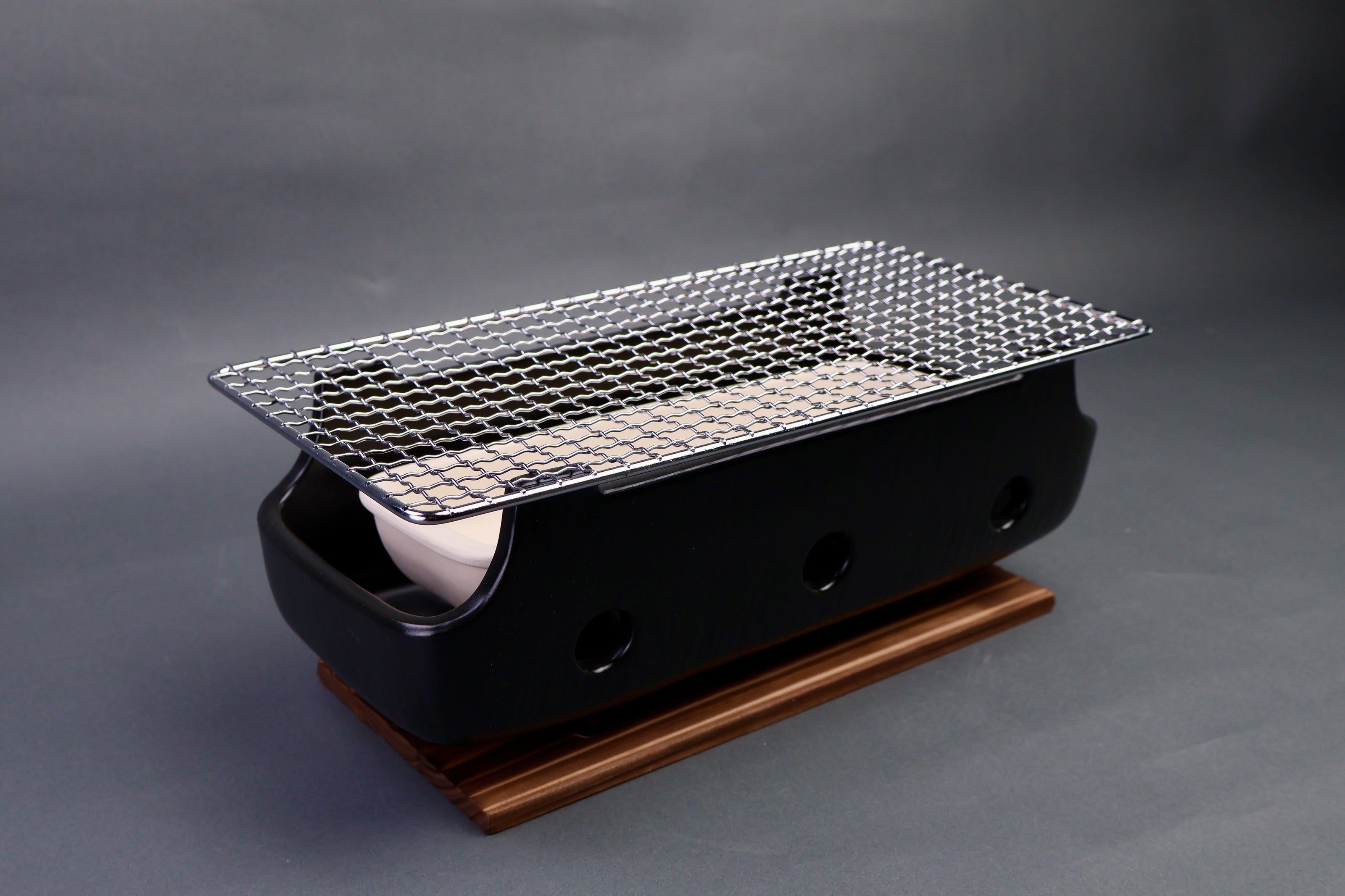 angled long back ceramic rectangular charcoal grill white tray interior stainless steel grill grate atop tan wood trivet in gray surrounding 