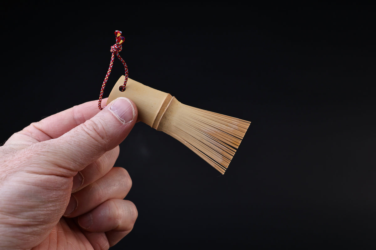 Yakumiyose bamboo brush held between fingers, bristle fringe extending to the side against a dark background