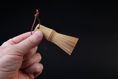 Yakumiyose bamboo brush held between fingers, bristle fringe extending to the side against a dark background