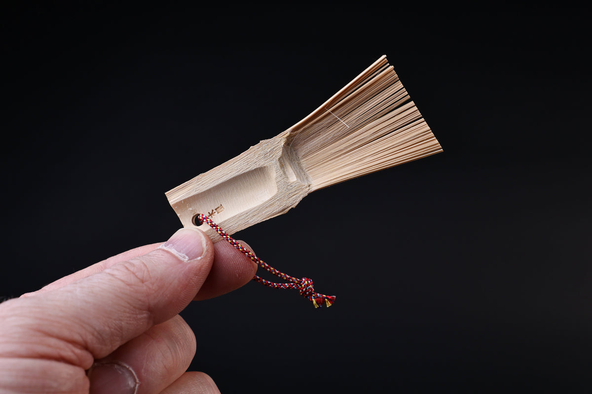Yakumiyose bamboo brush held to show the carved handle scoop, maker's stamp, and splayed bristles