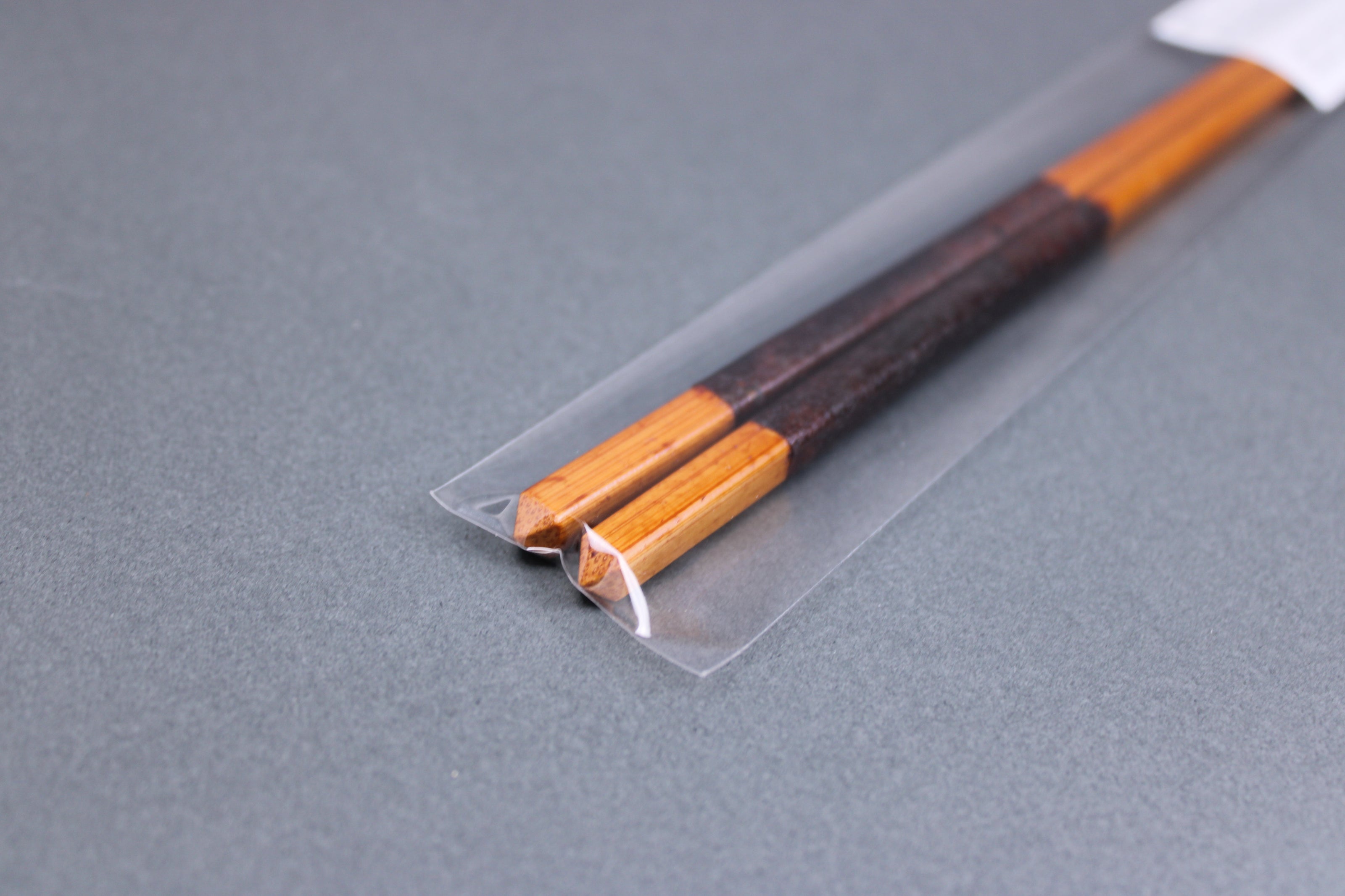 long square brownish tan bamboo cooking chopsticks urushi lacquered in clear packaging white product paper description in hiragana pointed end grey backdop