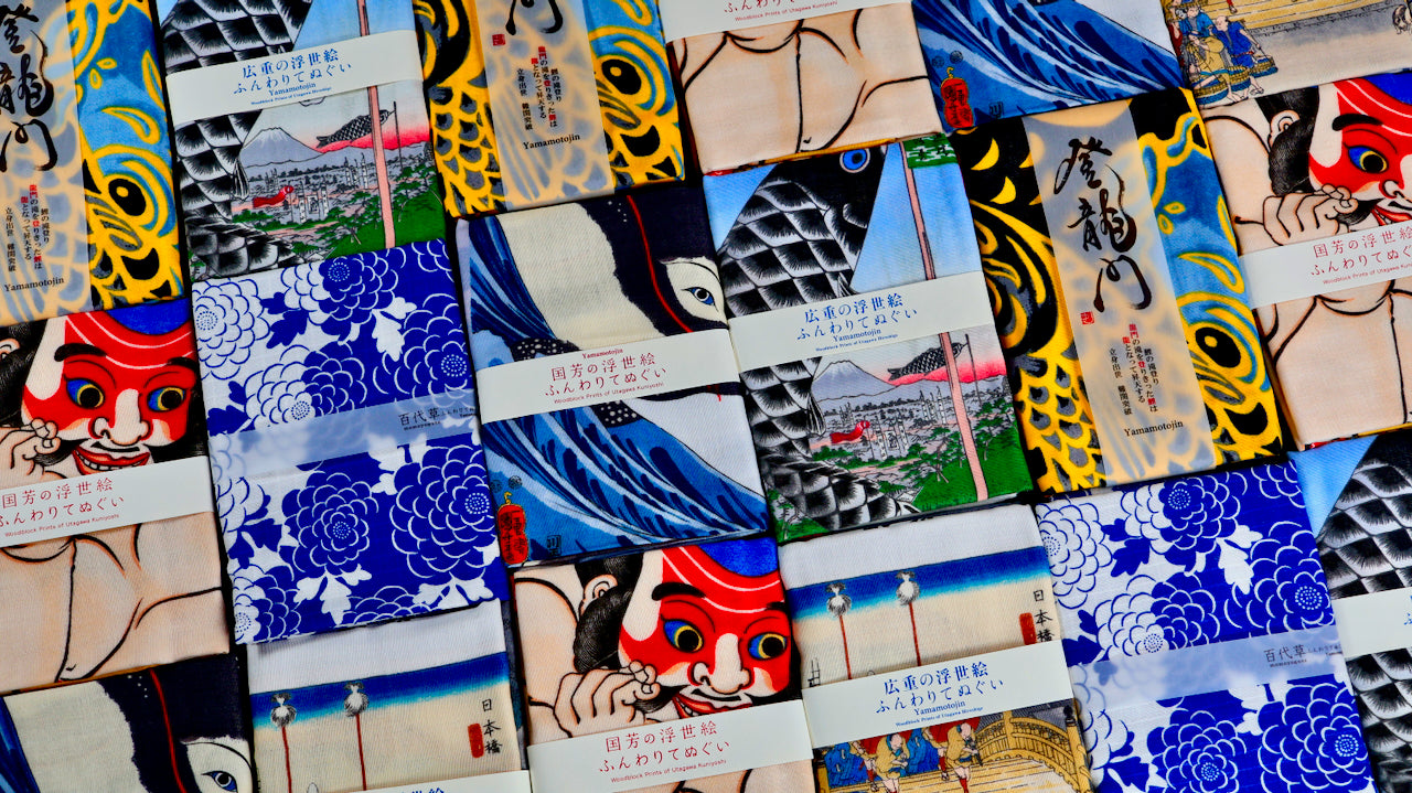 Collection of Yamamotojin tenugui hand towels in packaging showing ukiyo-e woodblock print designs including kabuki, koi, waves and peony patterns