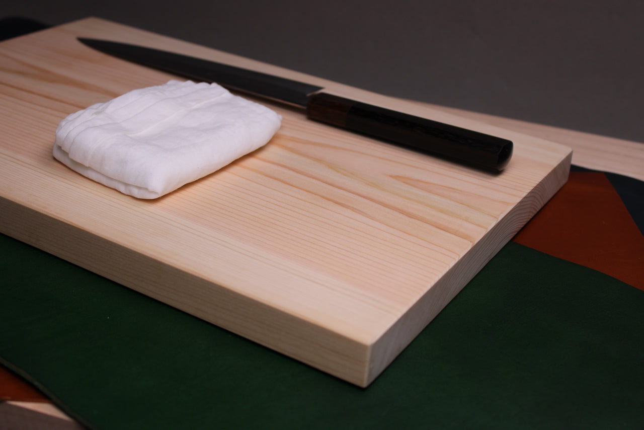 sarashi japanese kitchen towel displayed on hinoki cutting board beside 240mm gyuto knife with kitchen background