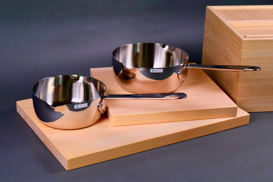 frontal shot of two steel shiny silver saucepans on top of two hinoki wood boards beside wood rice box in grey background 